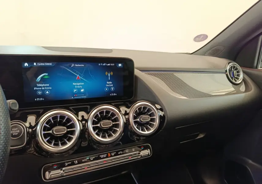 Vue intérieure côté passager du tableau de bord noir du Mercedes GLA 250 e AMG Line avec écran tactile et aérateurs ronds chromés.