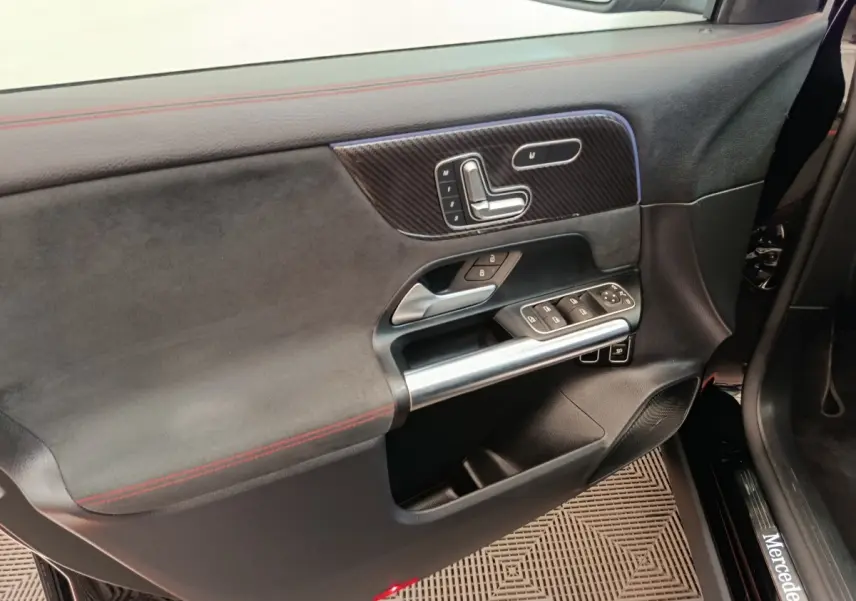 Vue intérieure côté conducteur de la porte noire du Mercedes GLA 250 e AMG Line avec surpiqûres rouges et commandes intégrées.