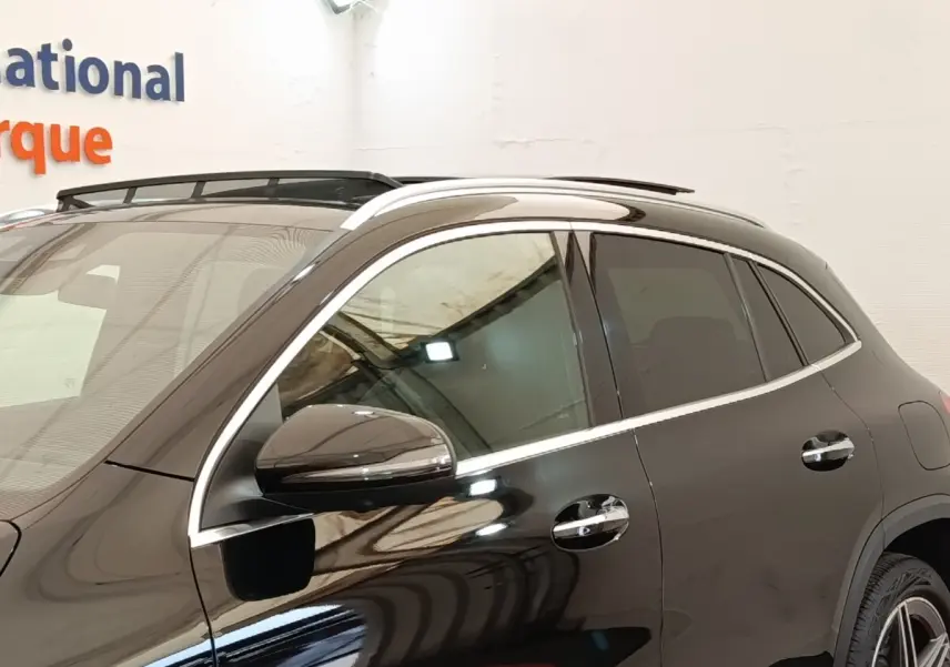 Vue latérale côté gauche d’un Mercedes GLA 250 e AMG Line noir brillant avec rails de toit chromés.