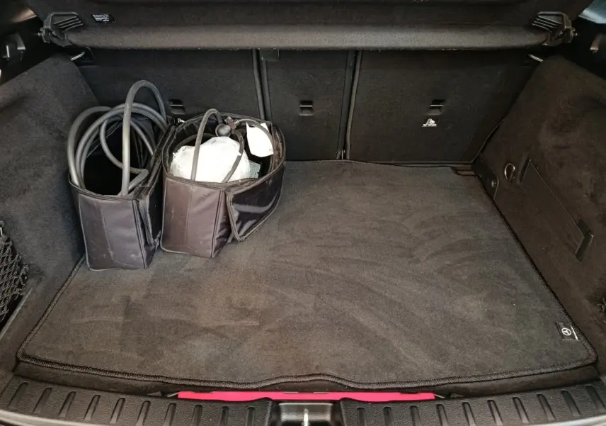 Coffre ouvert du Mercedes GLA 250 e AMG Line noir, vue plongeante montrant tapis et câbles de recharge rangés.