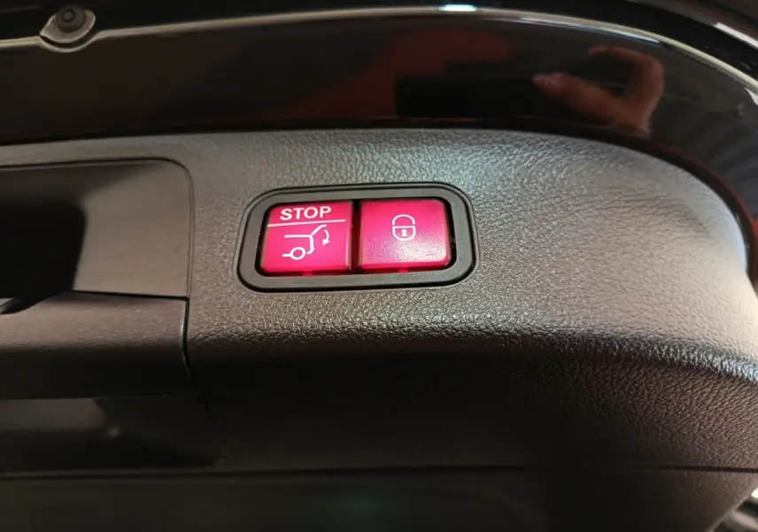 Boutons rouges d'ouverture et fermeture électrique du coffre sur la garniture intérieure noire d'un Mercedes GLA 250 e AMG Line.