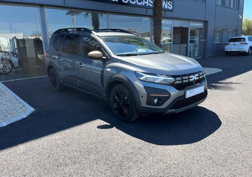 Dacia Jogger gris schiste en 3/4 avant droit, avec jantes noires et détails noirs sur la calandre et les bas de caisse.