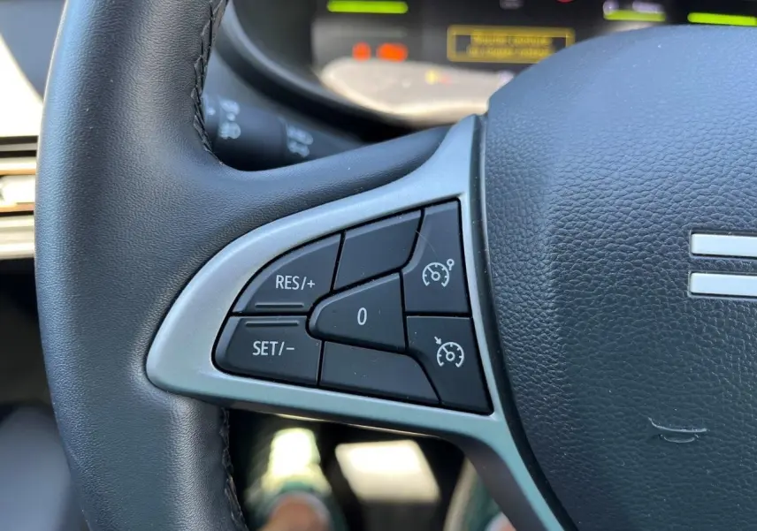 Gros plan sur les commandes de régulateur de vitesse au volant noir du Dacia Jogger 1.6 Hybrid gris schiste, version 2025.