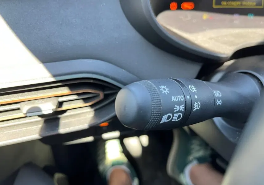 Gros plan sur la commande des phares du tableau de bord d’un Dacia Jogger gris schiste, intérieur lumineux.