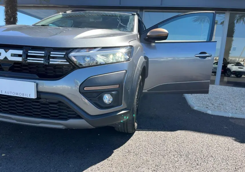 Vue avant droite du Dacia Jogger gris schiste 2025 avec porte ouverte et phares allumés, version hybride 7 places.