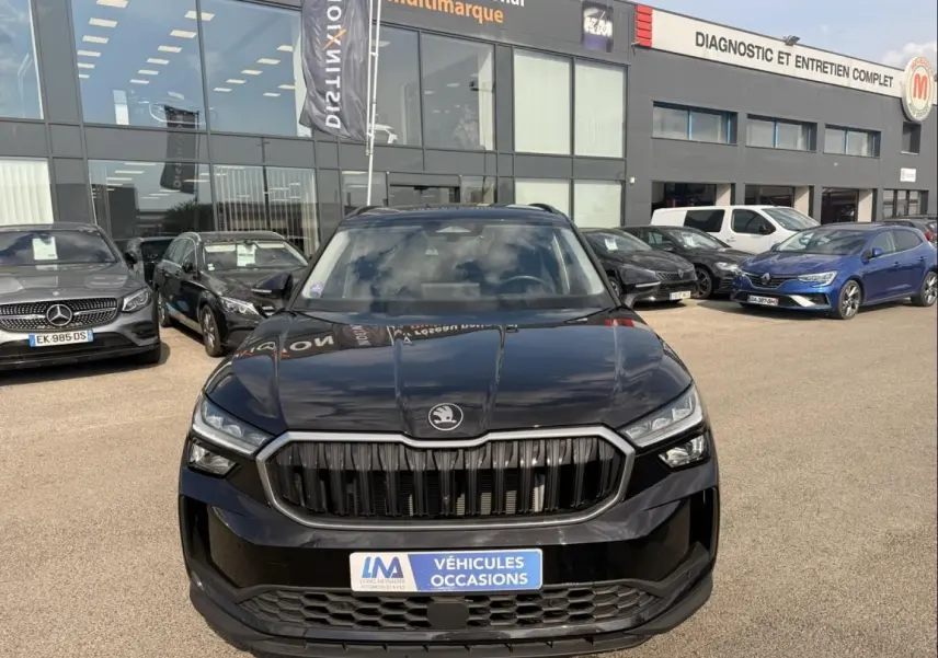 Vue avant d'un Skoda Kodiaq noir 2024 avec calandre verticale distinctive, stationné devant un garage multimarque.