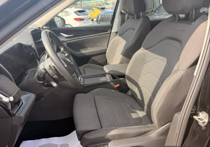 Intérieur avant droit du Skoda Kodiaq 2024 noir, sièges tissu gris et tableau de bord avec écran tactile.