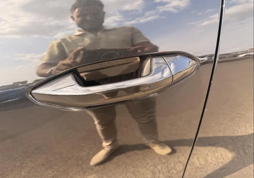 Poignée de porte chromée en gros plan sur une Skoda Kodiaq noire 2024, reflet d'une personne visible sur la carrosserie.