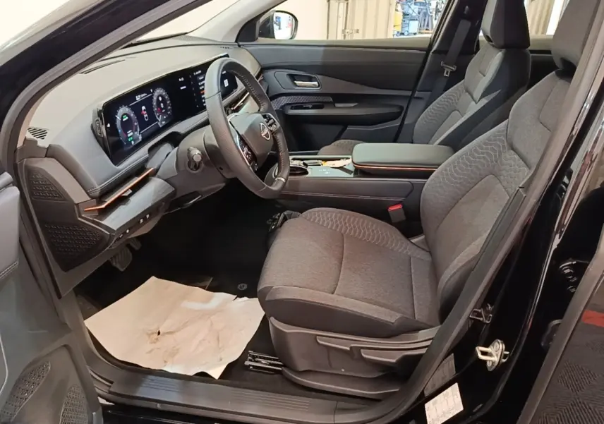 Vue intérieure côté conducteur du Nissan Ariya noir 2026, avec tableau de bord numérique et sièges gris tissu.