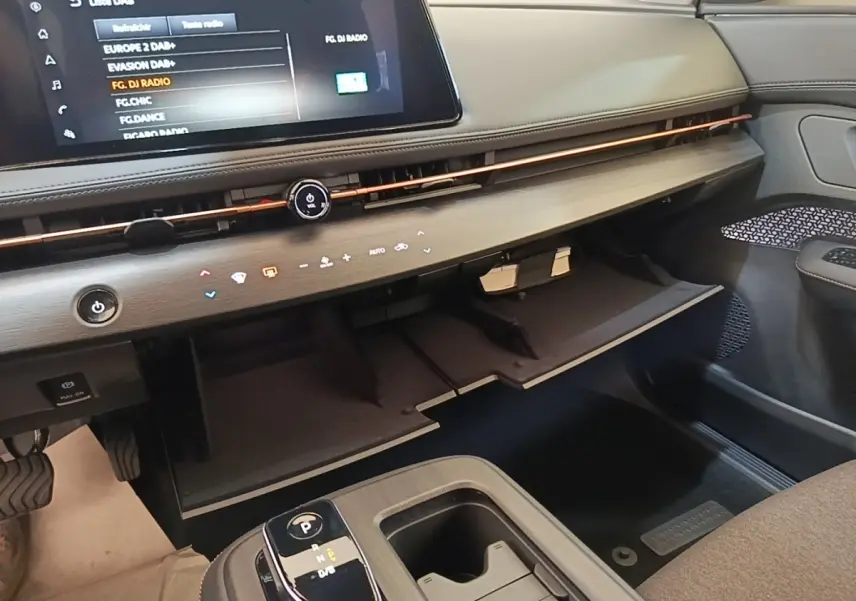 Vue intérieure côté passager du tableau de bord et boîte à gants ouverte du Nissan Ariya noir 2026 avec écran tactile.