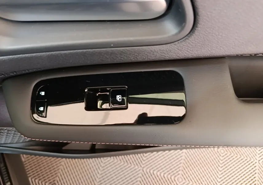 Gros plan sur la commande de lève-vitre côté conducteur du Nissan Ariya noir, avec finition brillante et surpiqûres rouges.
