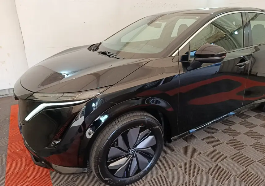 Vue 3/4 avant droit du Nissan Ariya noir avec phares LED et jantes au design moderne, stationné en intérieur.