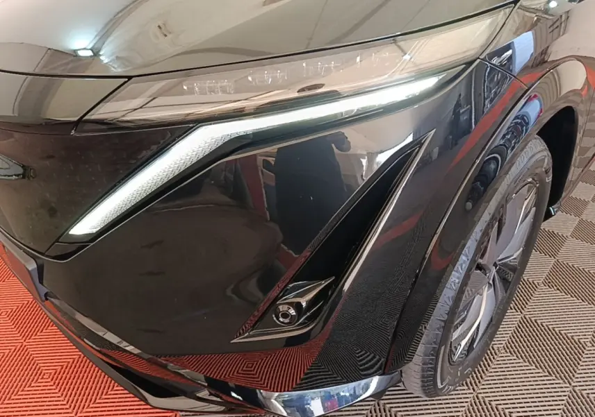 Gros plan sur l'avant droit noir brillant du Nissan Ariya 63kWh avec phares LED et jante moderne visible.