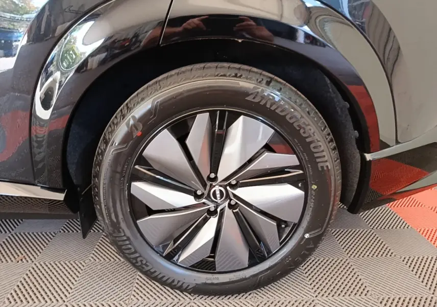 Gros plan sur la roue arrière droite noire du Nissan Ariya 63kWh avec jante argent et noire au design géométrique.