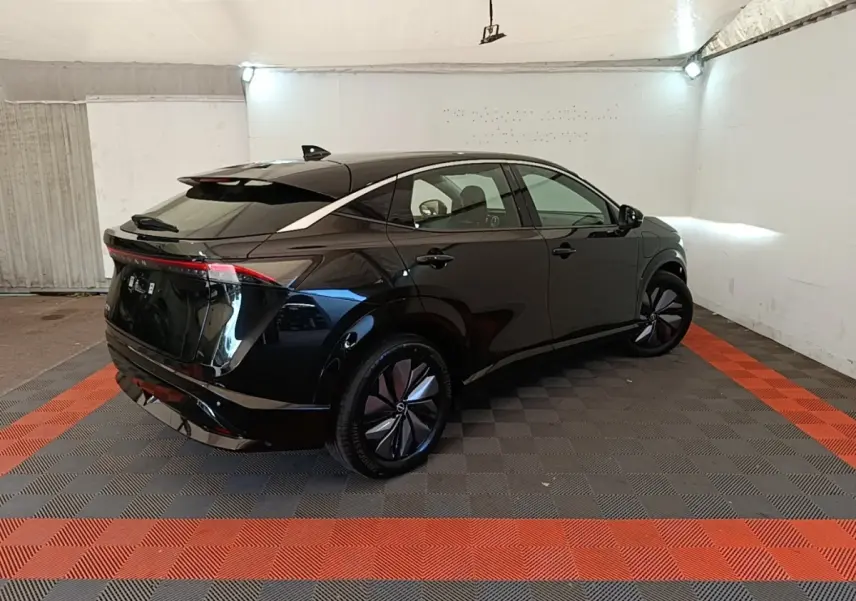 Nissan Ariya 63kWh noir en 3/4 arrière droit dans un garage, avec feux arrière continus et jantes stylisées.