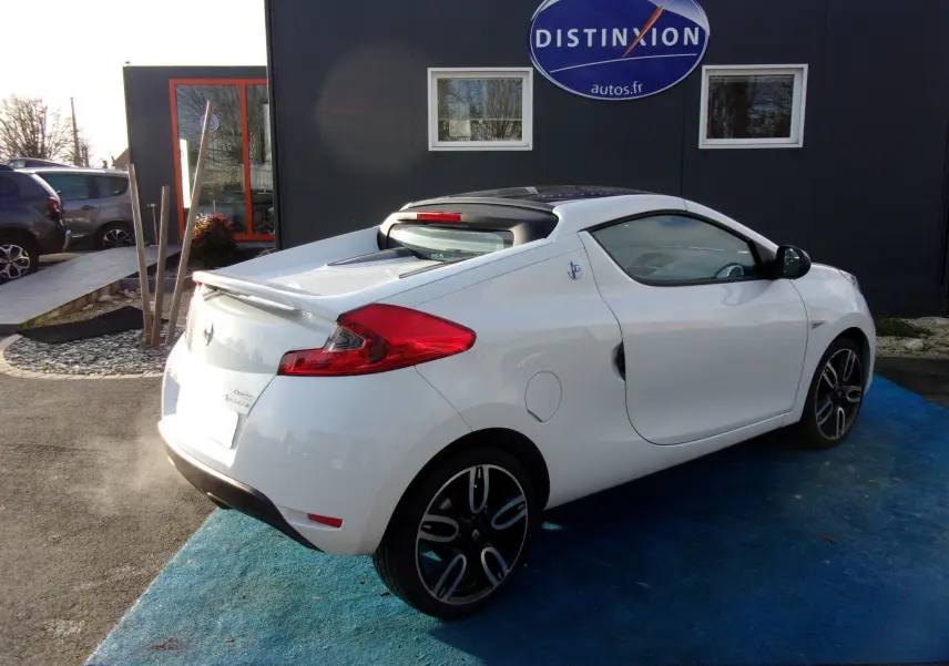 Vue 3/4 arrière droite d'une Renault Wind blanc glacier 2012 avec jantes noires et toit rigide rétractable.