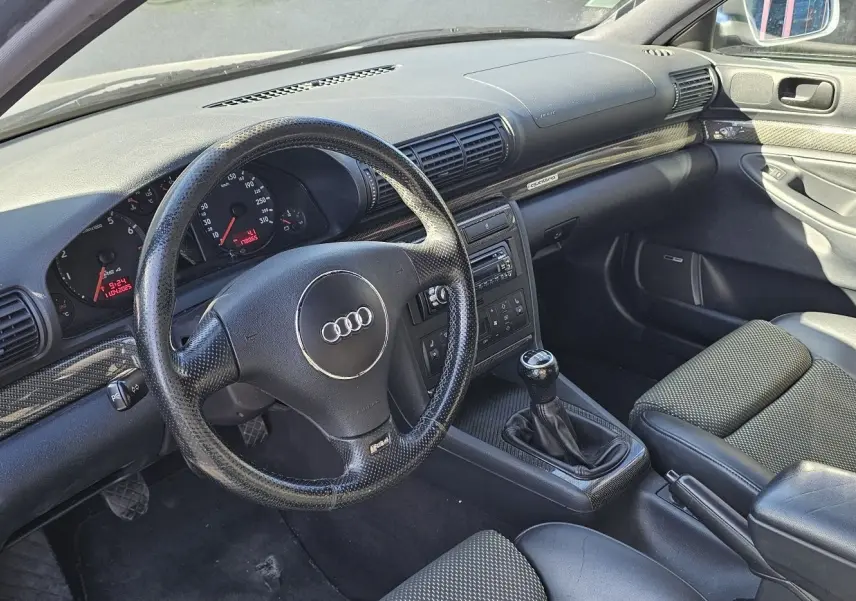 Intérieur noir de l'Audi RS4 Avant (B5) 2001, vue côté conducteur montrant volant, tableau de bord et levier de vitesses manuel.