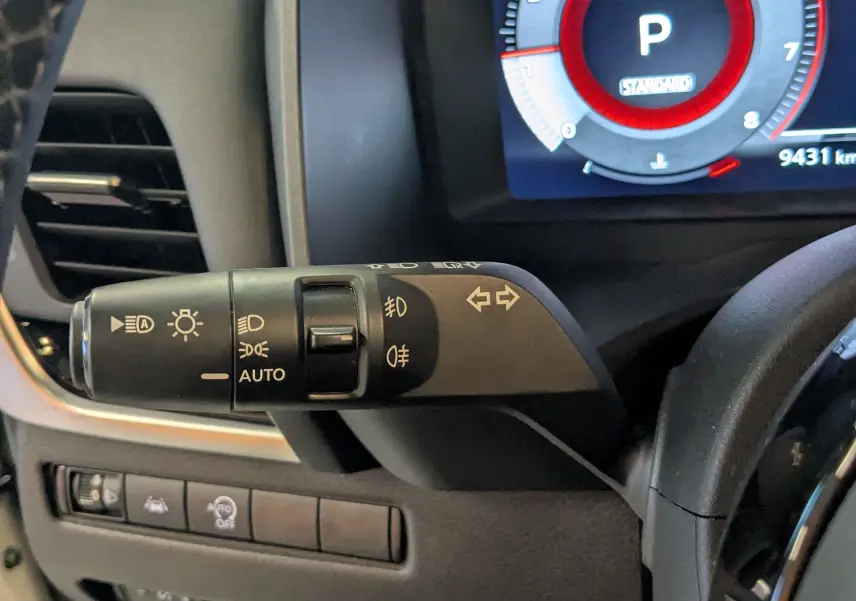 Gros plan sur la commande des feux et clignotants du Nissan Qashqai blanc 2024, tableau de bord numérique visible.