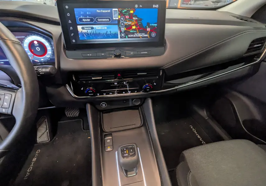 Vue intérieure du tableau de bord du Nissan Qashqai 2024 blanc, avec écran tactile central et levier de vitesse automatique.