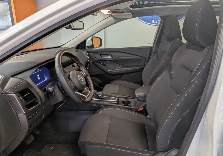 Vue intérieure côté conducteur du Nissan Qashqai blanc 2024, sièges noirs et tableau de bord moderne avec écran digital.