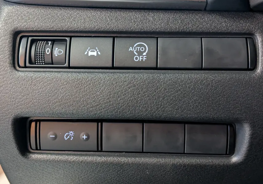 Gros plan sur les commandes noires du tableau de bord du Nissan Qashqai blanc 2024, avec réglage phares et assistance conduite.