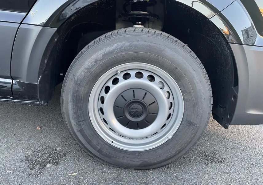 Gros plan sur la roue avant gauche du Volkswagen Crafter Van noir intense, mettant en valeur la jante acier et le logo VW central.