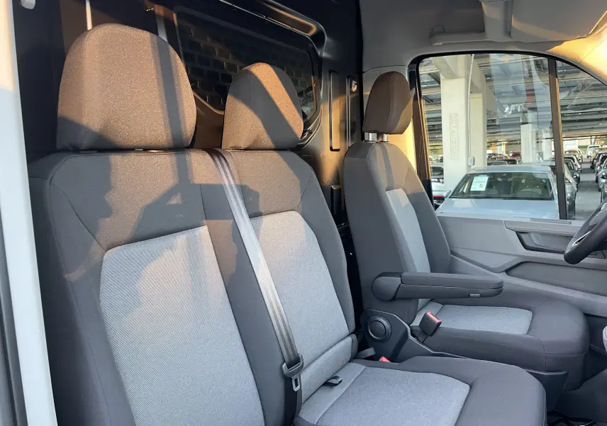 Vue intérieure côté conducteur du Volkswagen Crafter Van 2025, sièges gris et cloison métallique noire avec vitre fixe.
