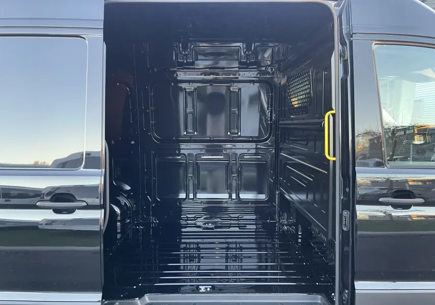 Vue intérieure du compartiment de chargement ouvert d'un Volkswagen Crafter Van noir intense, montrant la cloison avec vitre fixe.