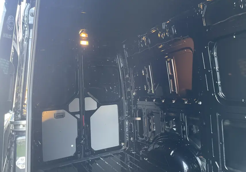 Intérieur du Volkswagen Crafter Van noir intense vu de l'arrière, montrant la cloison avec vitre fixe et parois métalliques.