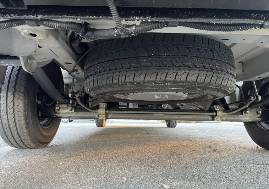 Vue en contre-plongée sous un Volkswagen Crafter Van noir intense, montrant la roue de secours et le train arrière.