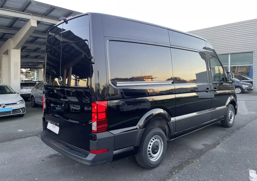 Vue 3/4 arrière droite d'un Volkswagen Crafter Van noir intense garé, avec vitres teintées et feux arrière rouges visibles.