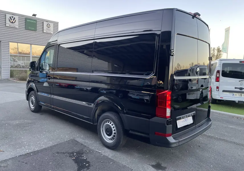 Vue 3/4 arrière côté droit d'un Volkswagen Crafter Van noir intense, avec vitres arrière teintées et feux LED visibles.