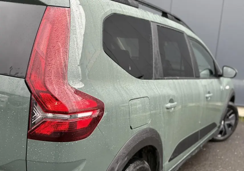 Vue 3/4 arrière droite d'un Dacia Jogger 2025 en Kaki Lichen avec feux arrière LED et barres de toit noires.