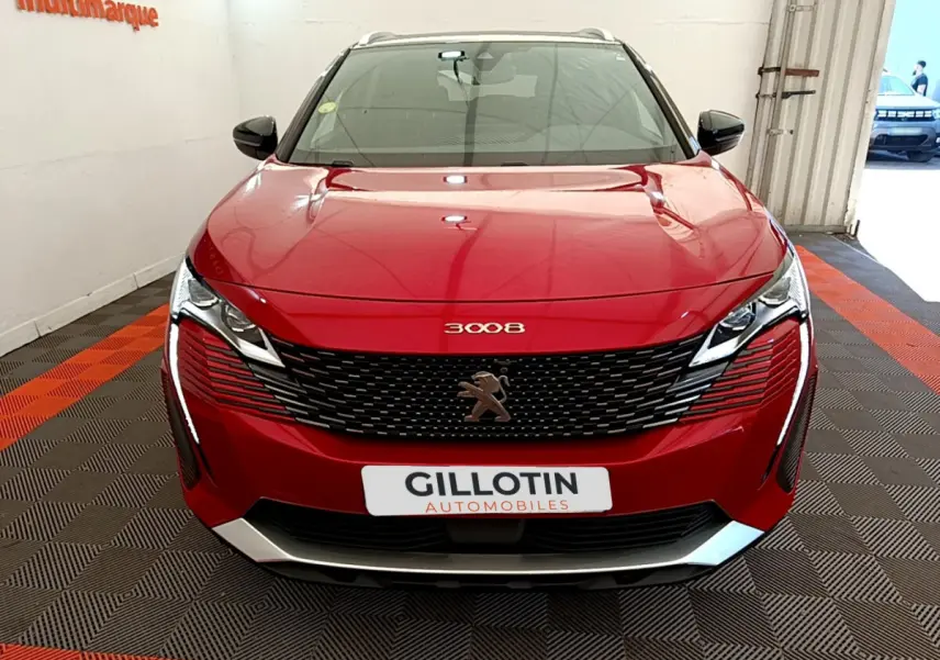 Vue frontale d'un Peugeot 3008 rouge avec calandre noire et logo lion central, dans un showroom intérieur.