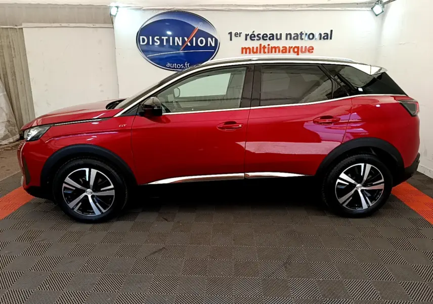 Profil côté gauche d’un SUV Peugeot 3008 GT rouge avec toit noir et jantes alliage bicolores, en intérieur showroom.