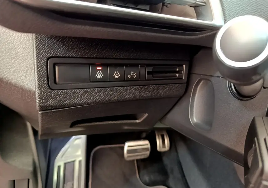 Détail intérieur côté gauche du tableau de bord du Peugeot 3008 rouge, avec commandes d'aide à la conduite et pédales en aluminium.