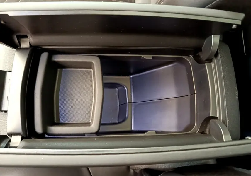 Vue plongeante sur le rangement central noir ouvert du Peugeot 3008 GT rouge, intérieur sobre et fonctionnel.