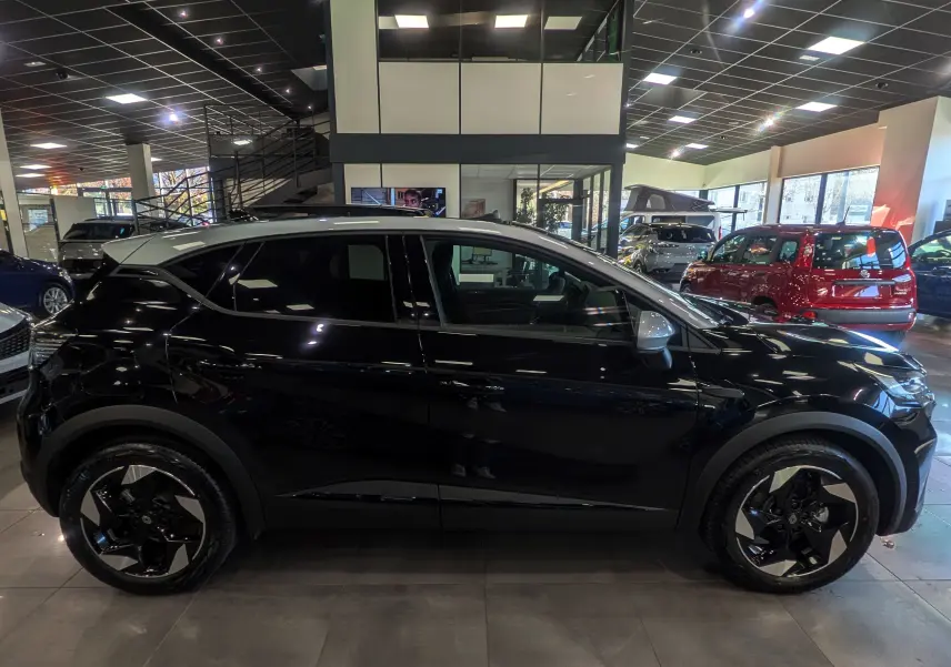 Profil côté gauche du Renault Captur E-TECH hybride noir avec toit gris Highland et jantes noires biton dans un showroom.