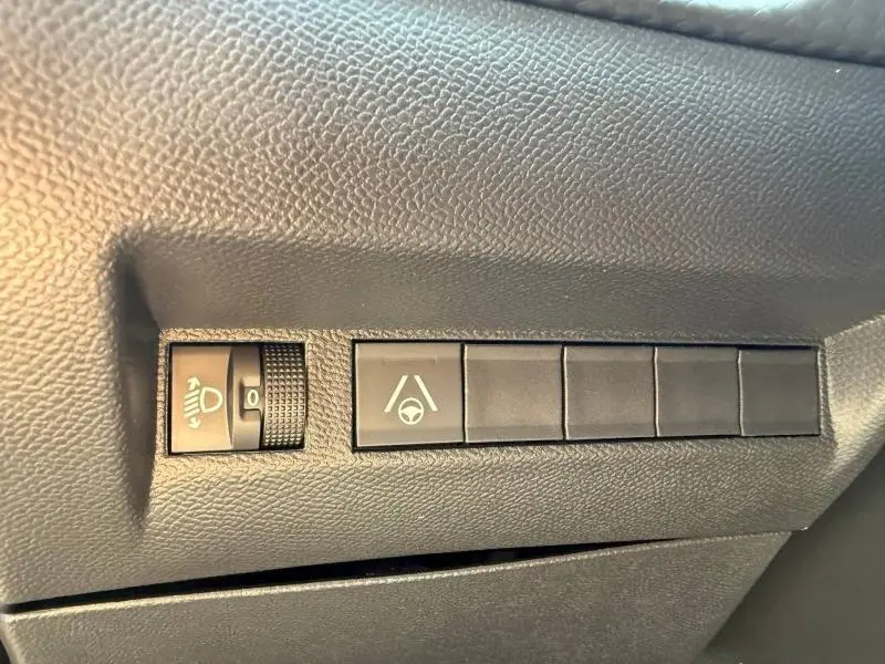 Gros plan sur les commandes d’aide à la conduite du Peugeot 2008 1.2 Hybrid 145ch Allure rouge, avec réglage des phares et assistance au maintien de voie.