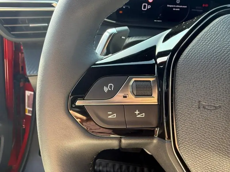 Gros plan sur les commandes gauche du volant du Peugeot 2008 Rouge Elixir 2025, avec boutons de volume et commande vocale.