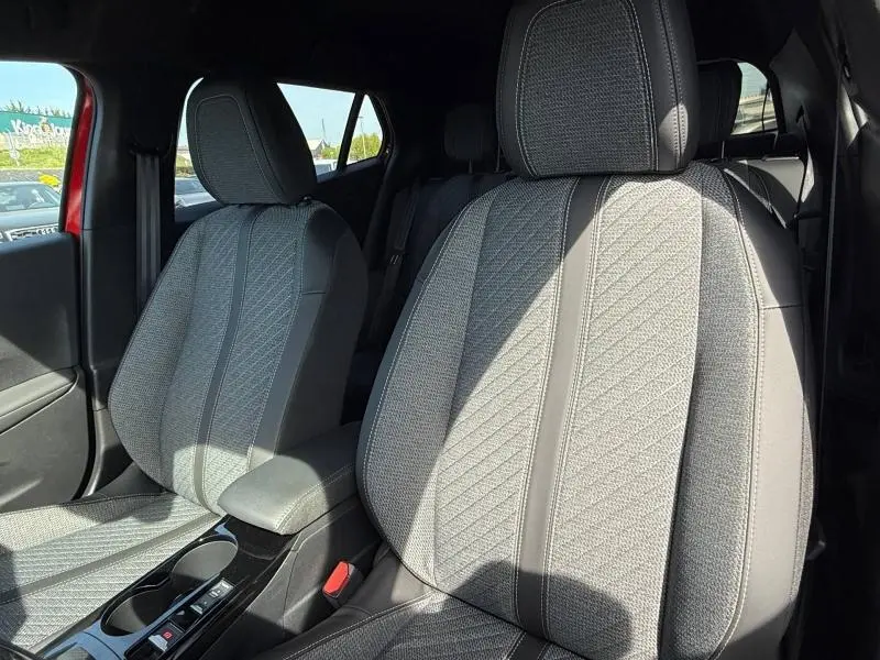 Gros plan sur les sièges avant gris texturés du Peugeot 2008 Rouge Elixir, intérieur lumineux avec accoudoir central visible.