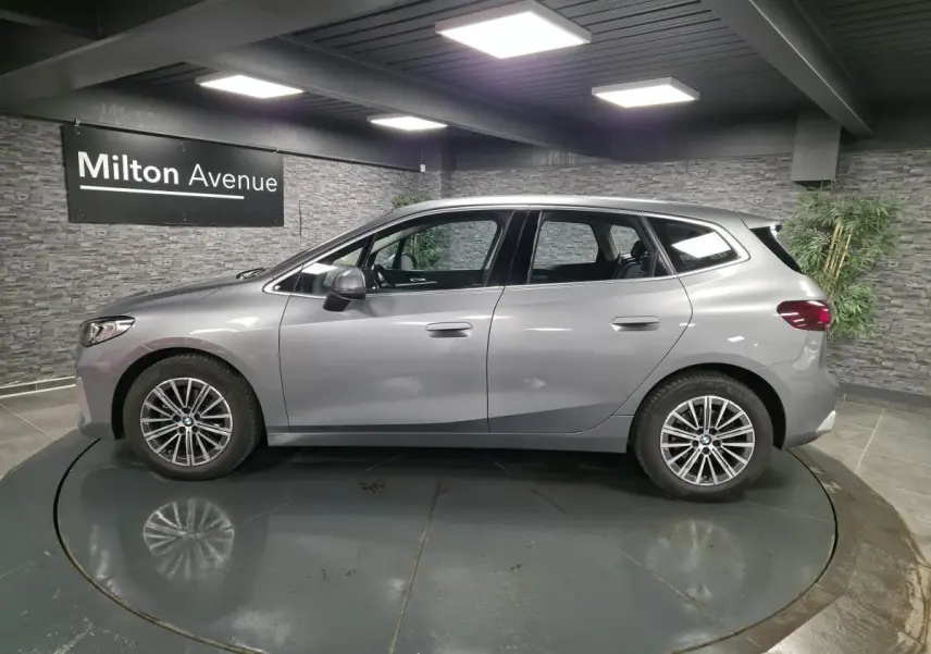 BMW Série 2 218d Active Tourer gris métallisé vue de profil côté gauche en intérieur showroom.
