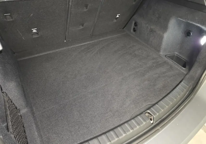 Coffre spacieux de BMW Série 2 218d gris, vue plongeante sur le plancher et les côtés garnis de moquette noire.