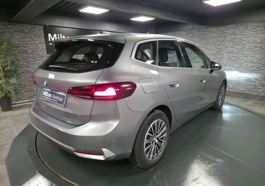 BMW Série 2 218d Active Tourer gris métallisé vue 3/4 arrière droit avec feux arrière allumés et jantes alliage 17 pouces.