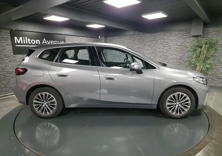 BMW Série 2 218d Active Tourer gris métallisé vue de profil côté gauche avec jantes alliage 17 pouces en intérieur showroom.