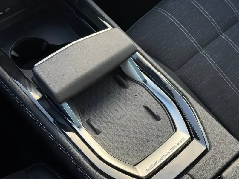 Gros plan sur la console centrale noire du Renault Austral 2025, avec repose-bras et surface de charge sans fil.