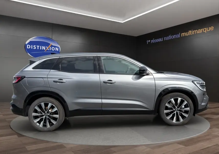 Profil droit d’un Renault Austral gris foncé avec jantes alliage bicolores, présenté en showroom intérieur.