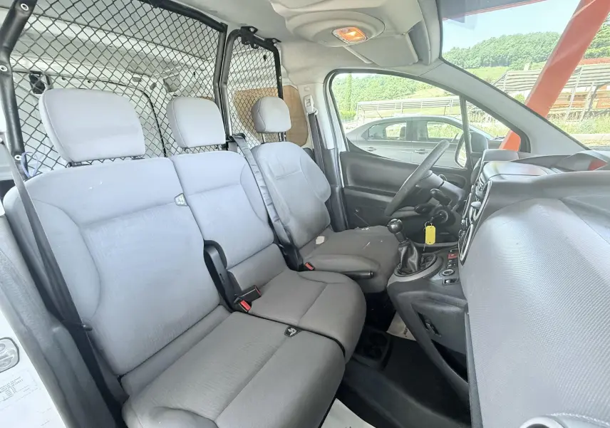 Intérieur côté droit du Peugeot Partner blanc 2014, montrant les sièges gris et la cloison métallique derrière.
