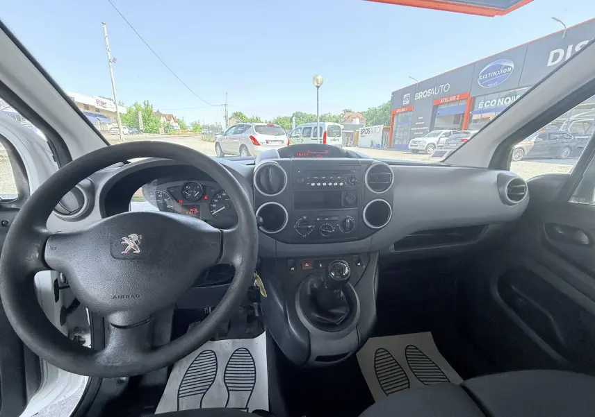 Vue intérieure avant du Peugeot Partner blanc 2014, montrant le volant, tableau de bord et levier de vitesses manuel.