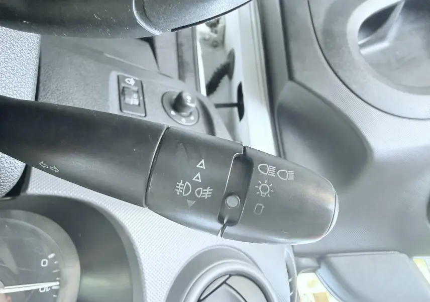 Gros plan sur la commande des phares et clignotants à gauche du volant dans l’habitacle gris du Peugeot Partner blanc 2014.